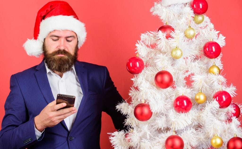 Uomo con cappello di Natale che usa lo smartphone, protezione dispositivi come regalo